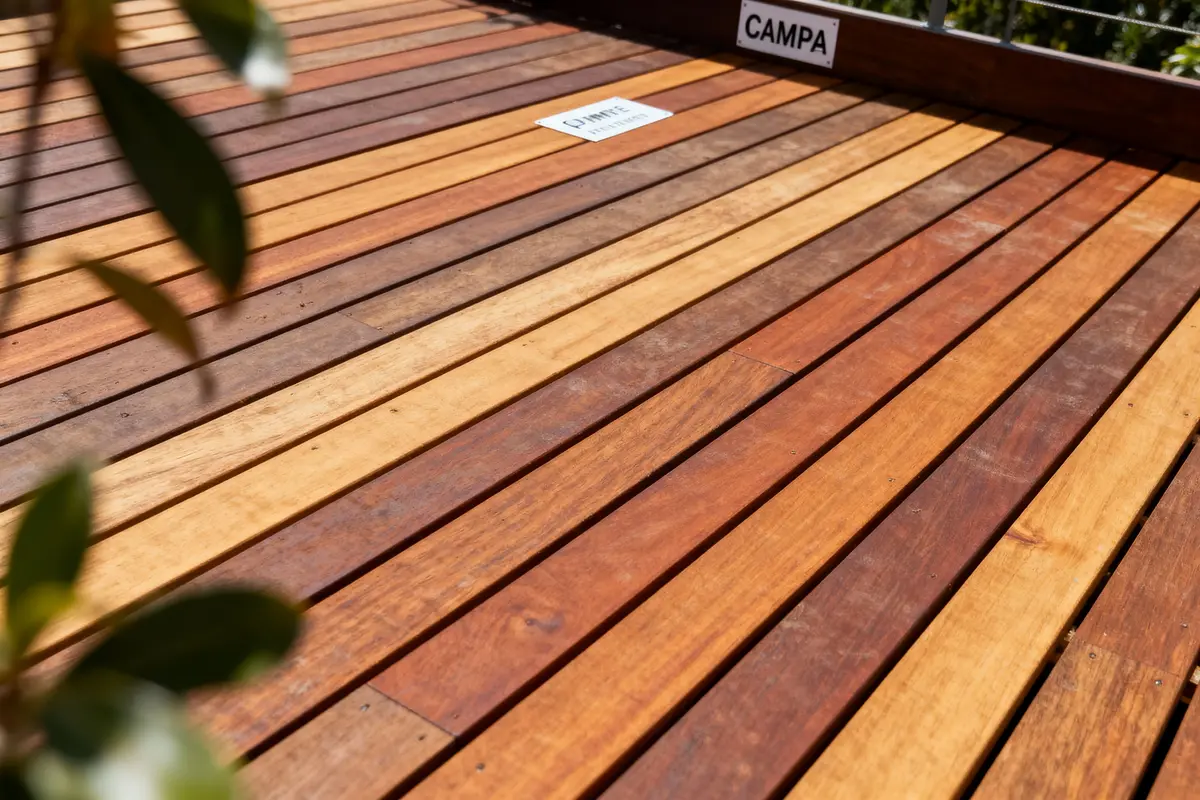 Planchers en bois de différentes teintes, avec une étiquette "CAMPA" visible, entourés de feuillage vert.