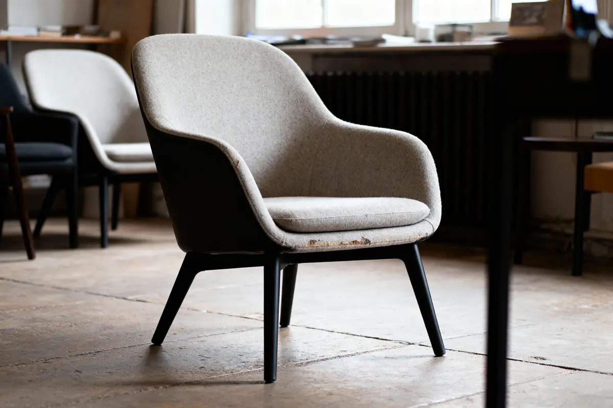 Fauteuil beige et noir moderne dans une pièce lumineuse avec parquet et fenêtre en arrière-plan.