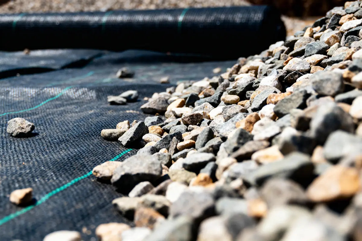 Graviers placés sur une bâche géotextile noire, rouleau de toile en arrière-plan.