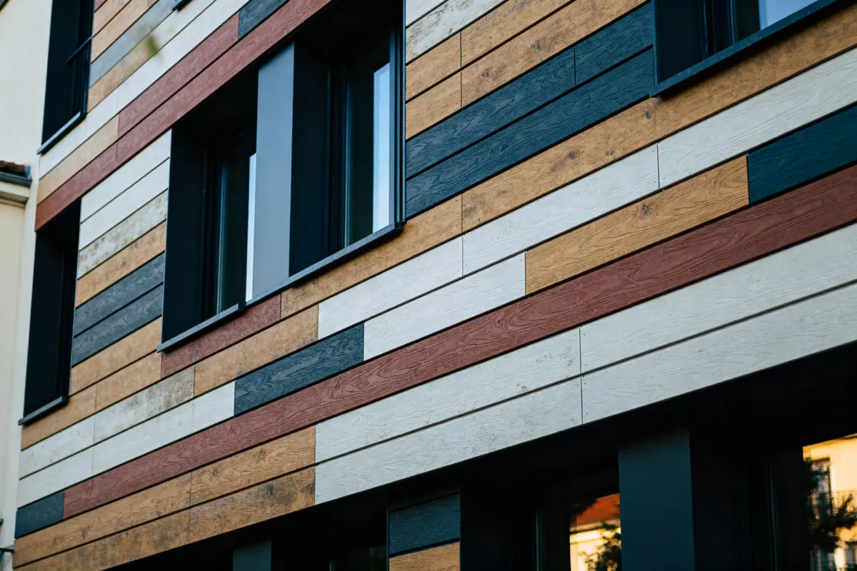 Façade d'immeuble moderne avec bardage en bois multicolore, grandes fenêtres noires, design contemporain attrayant.