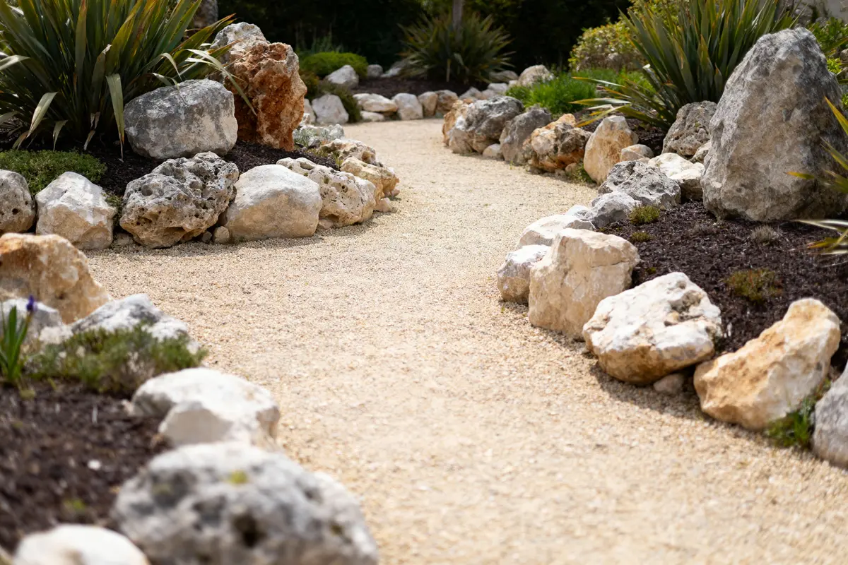 Allée de gravier bordée de rochers et de plantes vertes dans un jardin paysager.