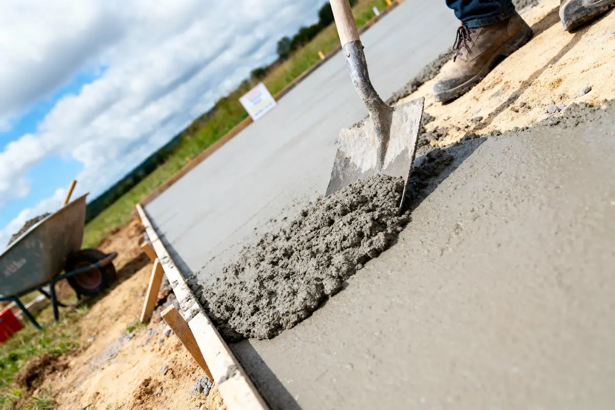 Une pelle étale du béton frais sur une dalle en construction, plein air.