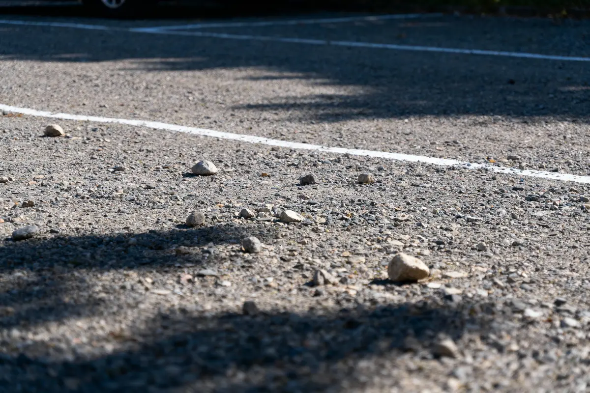 Surface de gravier avec petites pierres éparpillées, ombres visibles, lignes blanches délimitant zones.