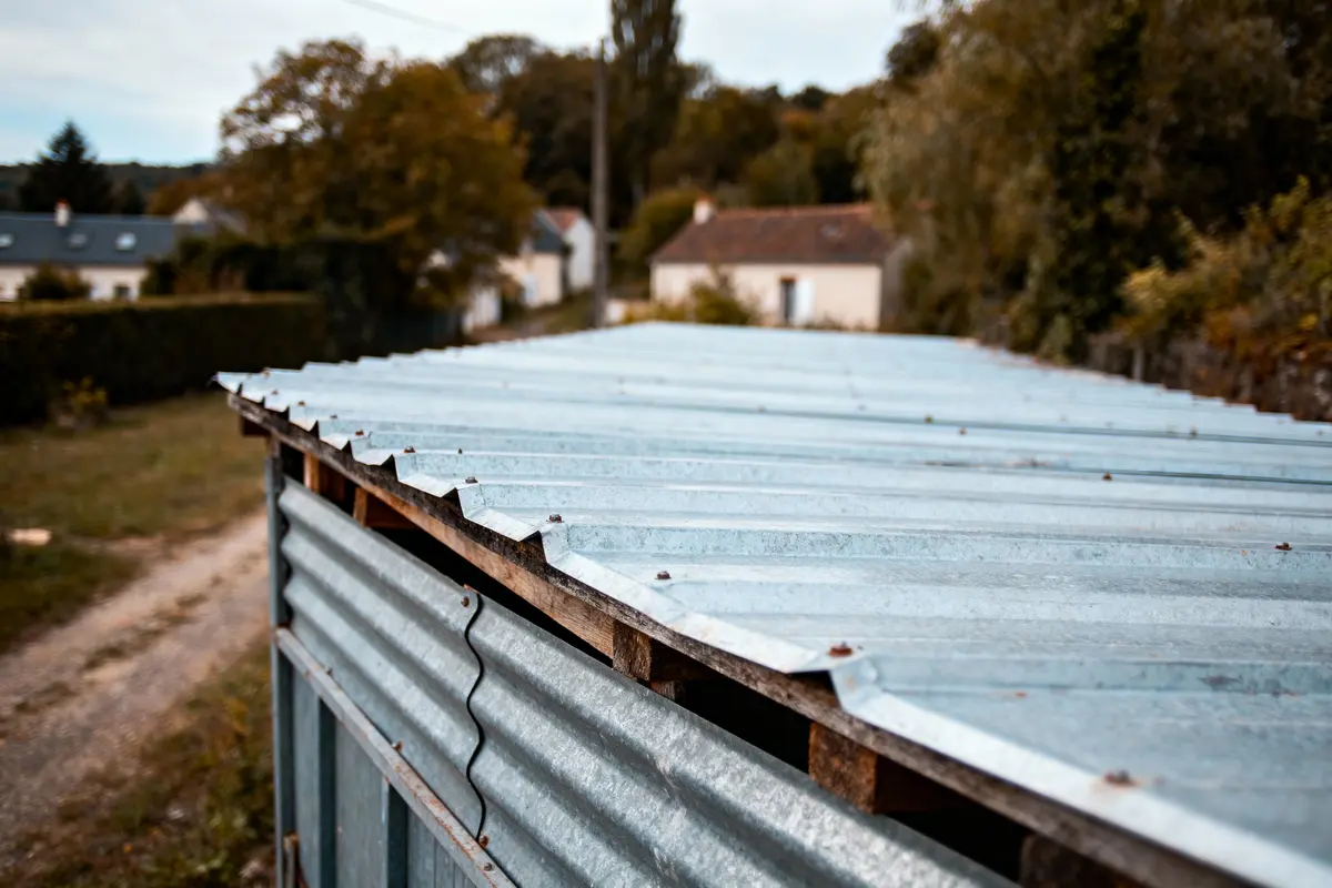 Toit en tôle ondulée d'un hangar à la campagne avec maisons et arbres en arrière-plan.