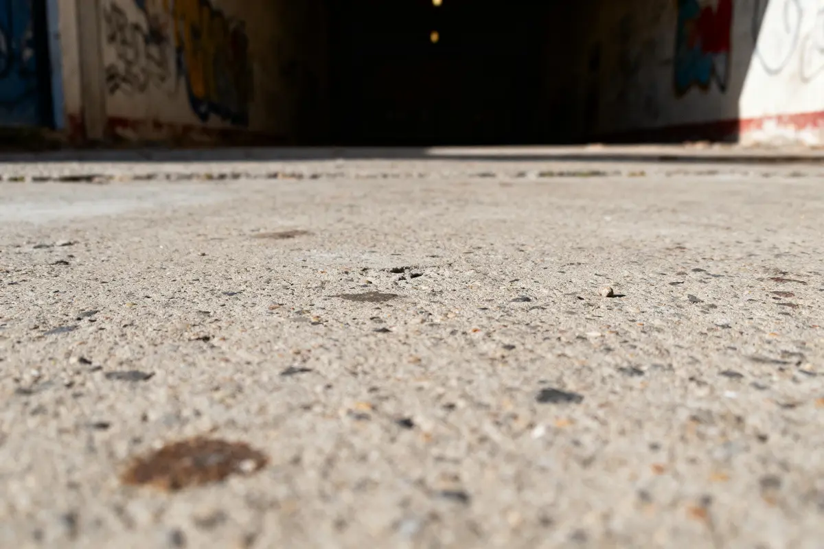 Sol en béton avec lumière floue au-dessus, murs graffitis, perspective vers une ouverture sombre.