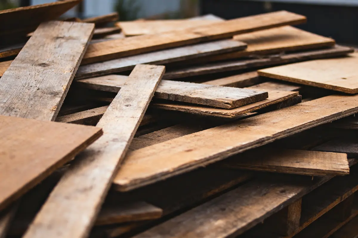 Planches de bois empilées de diverses tailles et textures, dans un environnement extérieur flou.