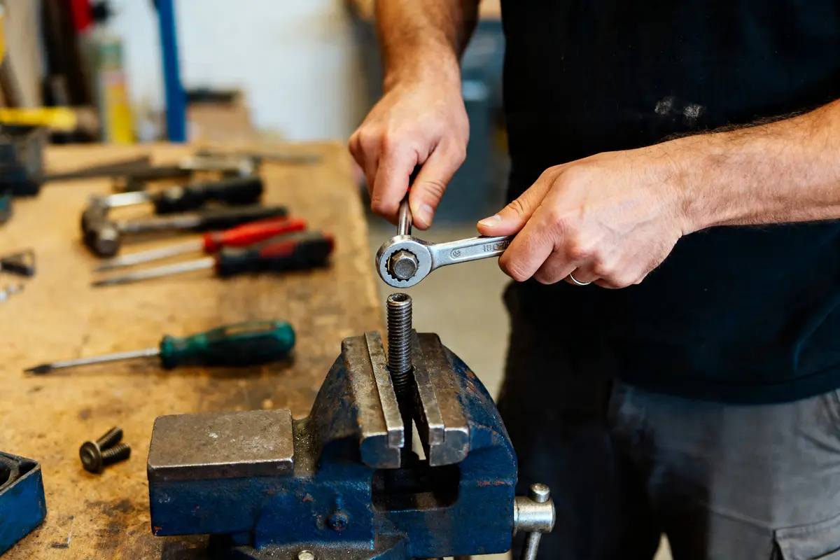 Homme utilisant une clé à molette pour dévisser un boulon maintenu par un étau