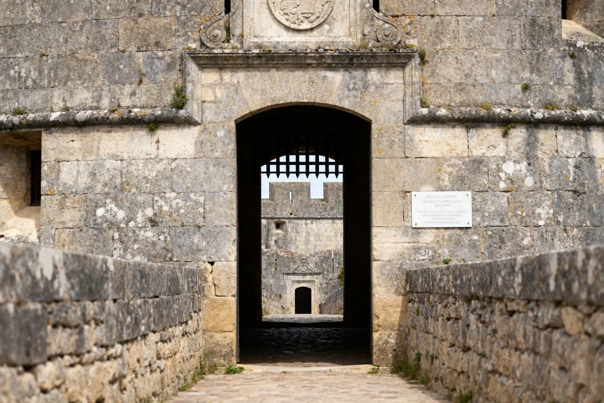 Entrée de château médiéval avec barbacane en pierre et fortifications visibles en arrière-plan